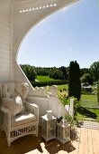 Wicker chair and lanterns in sheltered corner of exquisite wooden terrace with view of well-tended, landscaped garden