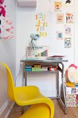 Yellow, child's chair at small desk below postcards and stamped numbers stuck to wall using washi tape