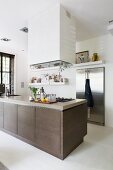 Island counter with brown base units below extractor hood in open-plan designer kitchen