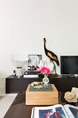 Wooden box and book on coffee table, vintage table lamp, stuffed bird and TV on sideboard in background