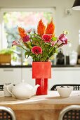 Vase of gerbera daisies and calla lilies in various shades of red in red vase on dining table