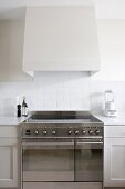 Detail of kitchen counter with modern stainless steel cooker with induction hob below white-clad extractor hood