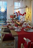 A festively laid Christmas table in red and white with a branch of Christmas ornaments hanging above it