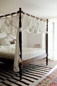 Antikes Himmelbett mit gedrechselten Bettpfosten und weißem, drapiertem Stoff in mediterranem Ambiente