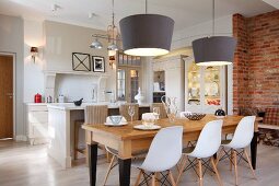 Classic chairs with white shell seats at wooden table below pendant lamps with grey, conical lampshades in front of white island counter in open-plan kitchen