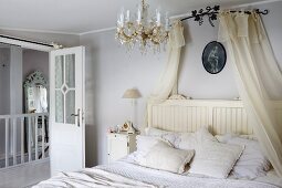 Schlafzimmer mit transparentem Baldachin über Doppelbett, offene Zimmertür mit Glasfüllung