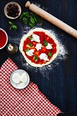 Ungebackene Pizza mit Tomaten, Mozzarella und Basilikum