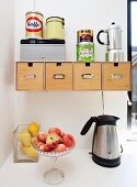Glass bowls of peaches and lemons next to kettle below wooden boxes in wall-mounted bracket with tin can and coffee maker on top