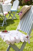 Romantisches geblümtes Sitzkissen auf hellgrauem Gartenstuhl mit Erdbeerteller und Sonnenhut dekoriert