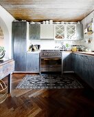 Einbauküche mit grauen Schrankoberflächen in schlichter Küche mit Vintage Teppich auf Fischgrätboden