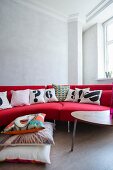 Bright red designer sofa with black and white scatter cushions and stacked cushions on floor in renovated period building with retro ambiance