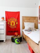 Rustic wood-framed bed with tall headboard next to red Manchester United flag hung on wall in boy's bedroom