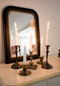 Still-life arrangement of lit candles in vintage crass candlesticks in front of mirror