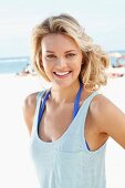 A young blonde woman on a beach wearing a blue tank top