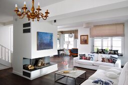 Open-plan interior with white sofas in front of open fireplace below blue modern artwork on free-standing chimney breast