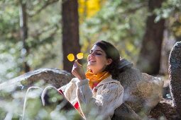 Woman in walking clothes leaning against boulder in autumnal woodland clearing