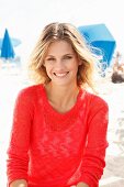 A young blonde woman on a beach wearing a transparent red knitted jumper