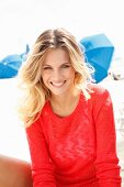 A young blonde woman on a beach wearing a transparent red knitted jumper