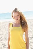 Blonde junge Frau in gelbem Sommerkleid am Strand