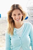 Junge blonde Frau in hellem Shirt und Strickjacke in Hellblau am Strand