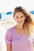 Junge blonde Frau in fliederfarbenem Kurzarm Shirt am Strand