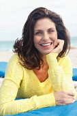 A brunette woman on a beach wearing a yellow knitted jumper resting her chin on her hand