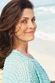 A brunette woman on a beach wearing a mint-coloured, openwork jumper