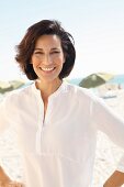 A brunette woman on a beach wearing a thin white blouse