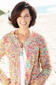 A brunette woman on a beach wearing a white top and colourful cardigan