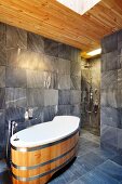 Designer bathroom with bathtub in modern, barrel design, grey tiles and open-plan shower in background