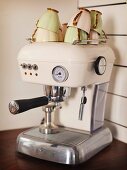 Cremefarbene Retro Espressomaschine mit gestapelten edlen Vintage Kaffeetassen auf Küchenarbeitsplatte