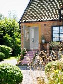 Blick von sonnenbeschienenem Garten auf Landhaus mit offener Haustür, davor Treppe mit Teppichläufer