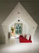 Holzverkleidete Nische in ausgebautem Dachgeschoss, auf weiss lackiertem Dielenboden rote Matratze und Kissen