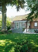 Grossgewachsener Baum im Garten vor Wohnhaus mit offenen Terrassentüren und breiter Treppe