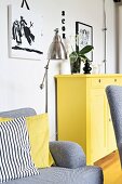 Sofa mit gemustertem und gelbem Kissen, im Hintergrund gelb lackierte Kommode an Wand