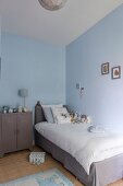 Single bed with grey valance and white bed linen next to retro metal cabinet in child's bedroom with pale blue walls