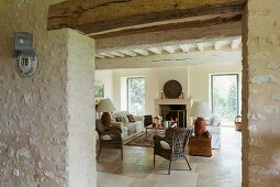 View through open doorway into renovated living room of Mediterranean country house with wicker chairs and sofa in front of fireplace