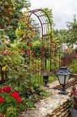 Torbogen aus Metall als Rankhilfe in sommerliche, ländlichem Garten mit Natursteinmauer