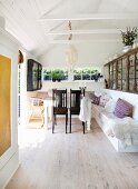 Dunkle Holzstühle vor Tisch und gemauerte Sitzbank weiss gestrichen in schlichtem Sommerhaus