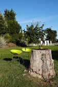 Baumstamm als Gartentisch mit zwei neongelben Barhockern in sommerlichem Garten