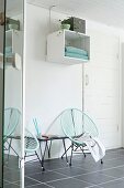 Retro Sessel mit türkiser Seilverspannung auf grauem Fliesenboden, vor Wand mit aufgehängtem Regalmodul
