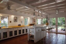 Langgestreckte Küchenzeile und gemauerte Frühstückstheke mit Drahthockern unter weiss lackierter Holzbalkendecke