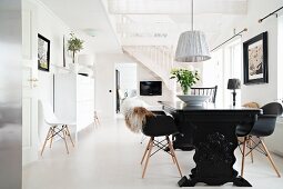 Solid-wood dining table painted black and classic shell chairs below pendant lamp with fabric lampshade