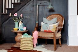 Antique armchair with scatter cushions next to seagrass stool and round stone table