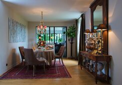 Upholstered chairs around set dining table on Oriental rug and table lamps on antique console table below mirror