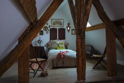 View of bed between rustic wooden beams in converted attic with pitched roof