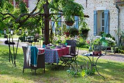 Gedeckter Gartentisch mit Stühlen aus Rattan und Metall, nostalgische Windlichter und Kerzenhalter