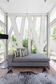 Grey chaise against unusual steel and glass façade on wooden floor with animal-skin rug