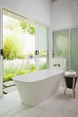 Free-standing bathtub in modern bathroom with open sliding door leading to terrace