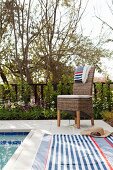 Striped towels on wicker chair and tiled edge of pool in garden